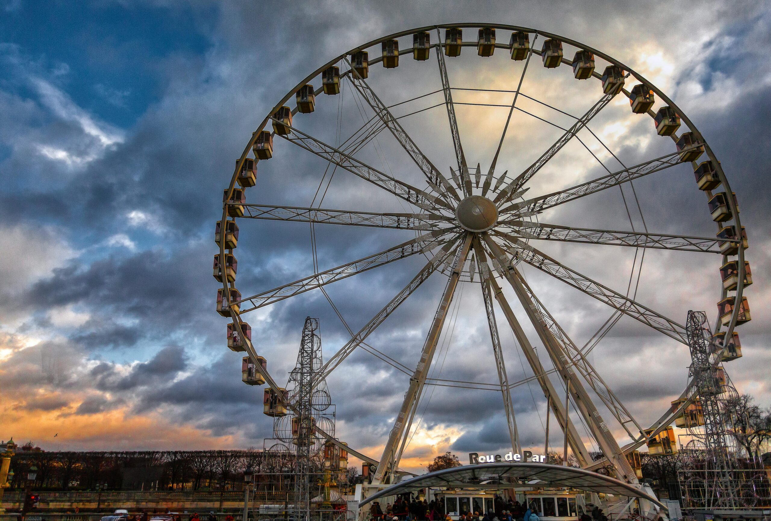 A stunning ferris wheel in a theme park with a dramatic cloudy sky backdrop.